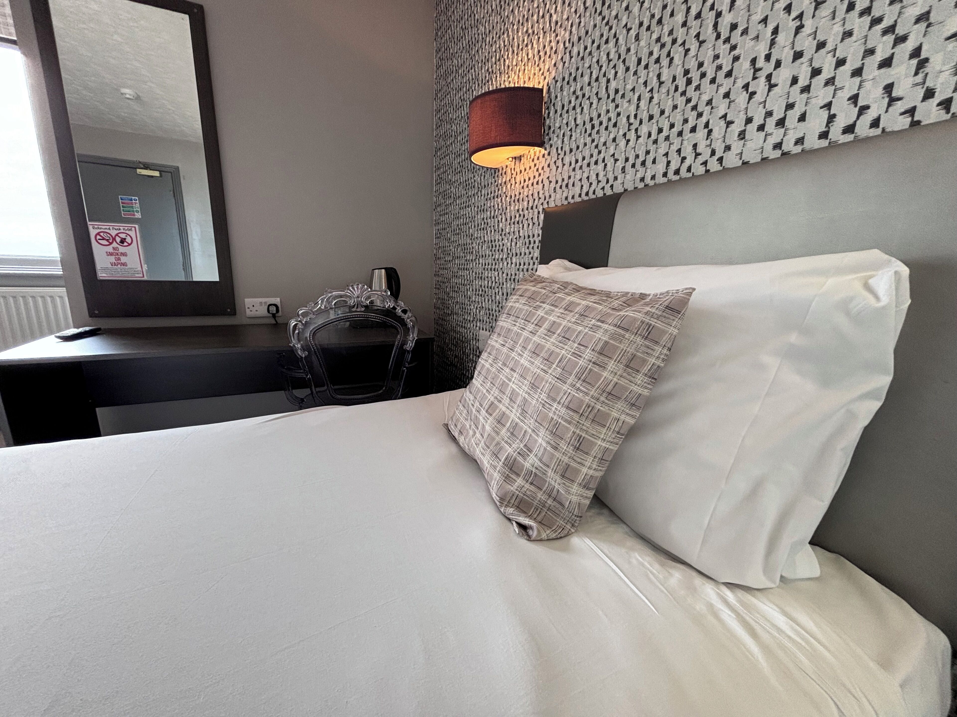 Ein Hotelzimmer mit Bett, Nachttisch, Lampe und Spiegel.