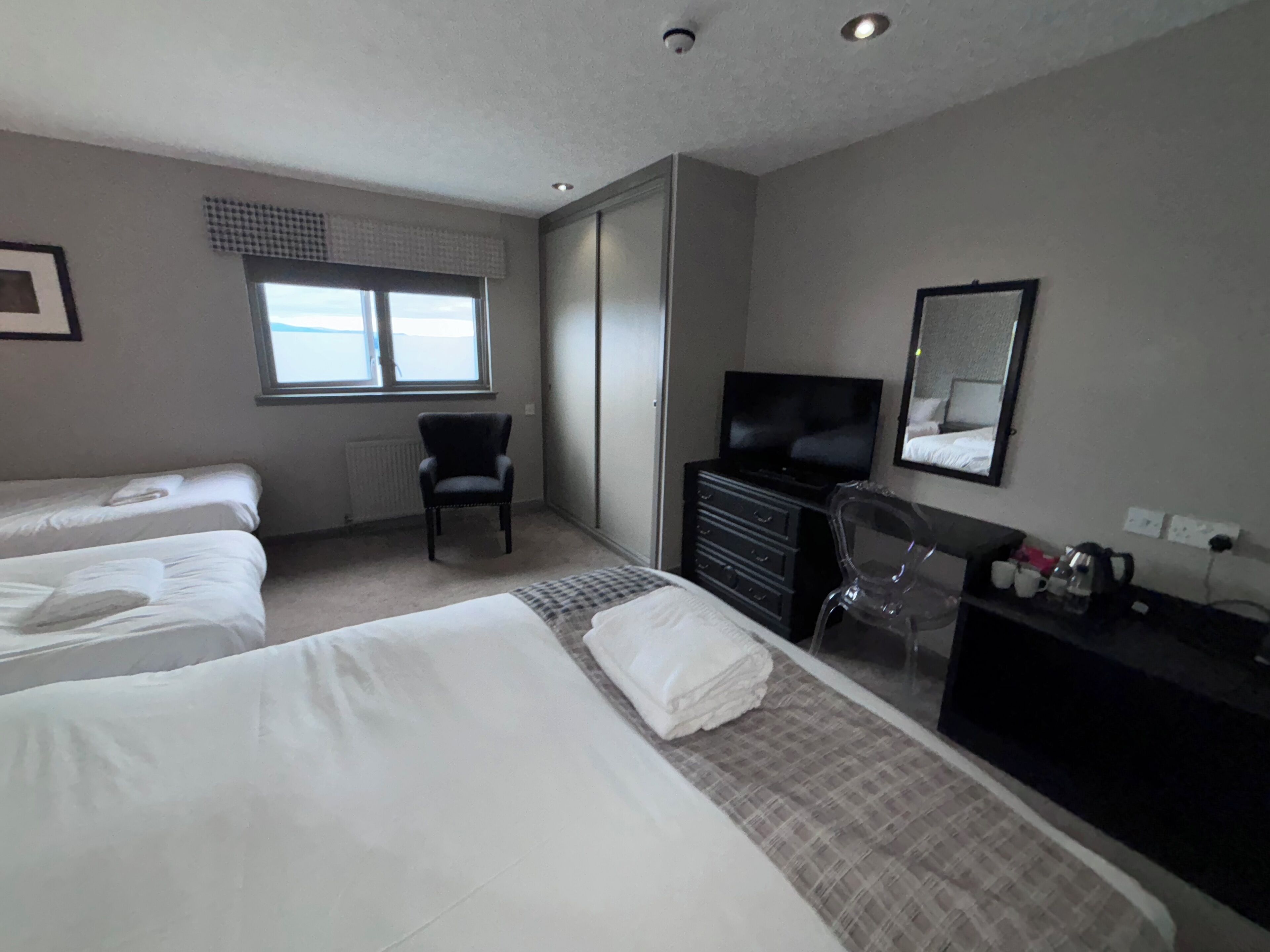 A hotel room with two beds, a chair, a dresser, a television, and a window with blinds.