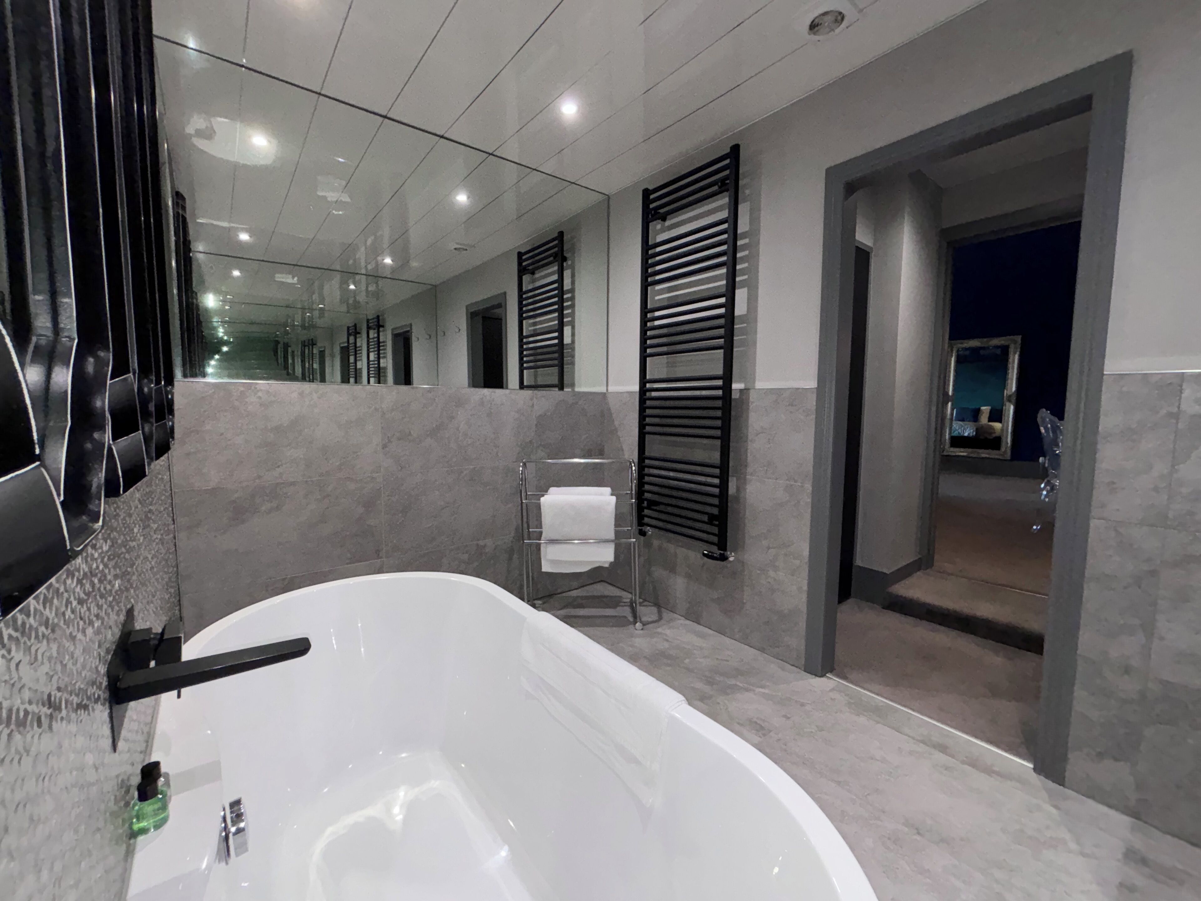 Een moderne badkamer met een groot bad, een douchecabine van glas en een spiegel die de ruimte weerspiegelt.