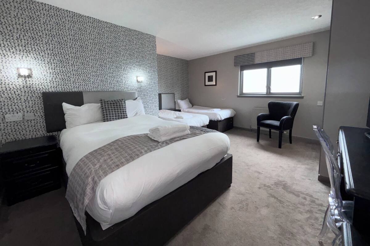 Ein modernes Hotelzimmer mit einem großen Bett, zwei Nachttischen, einem Sessel und einem Fenster.