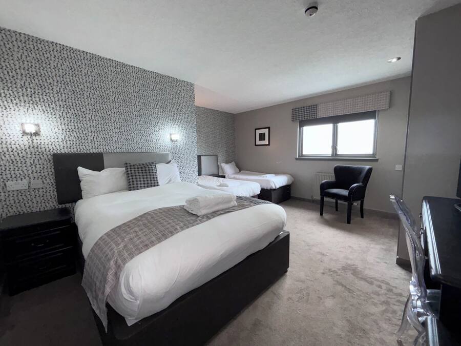 A modern hotel room with a large bed, two bedside tables, a chair, and a window.
