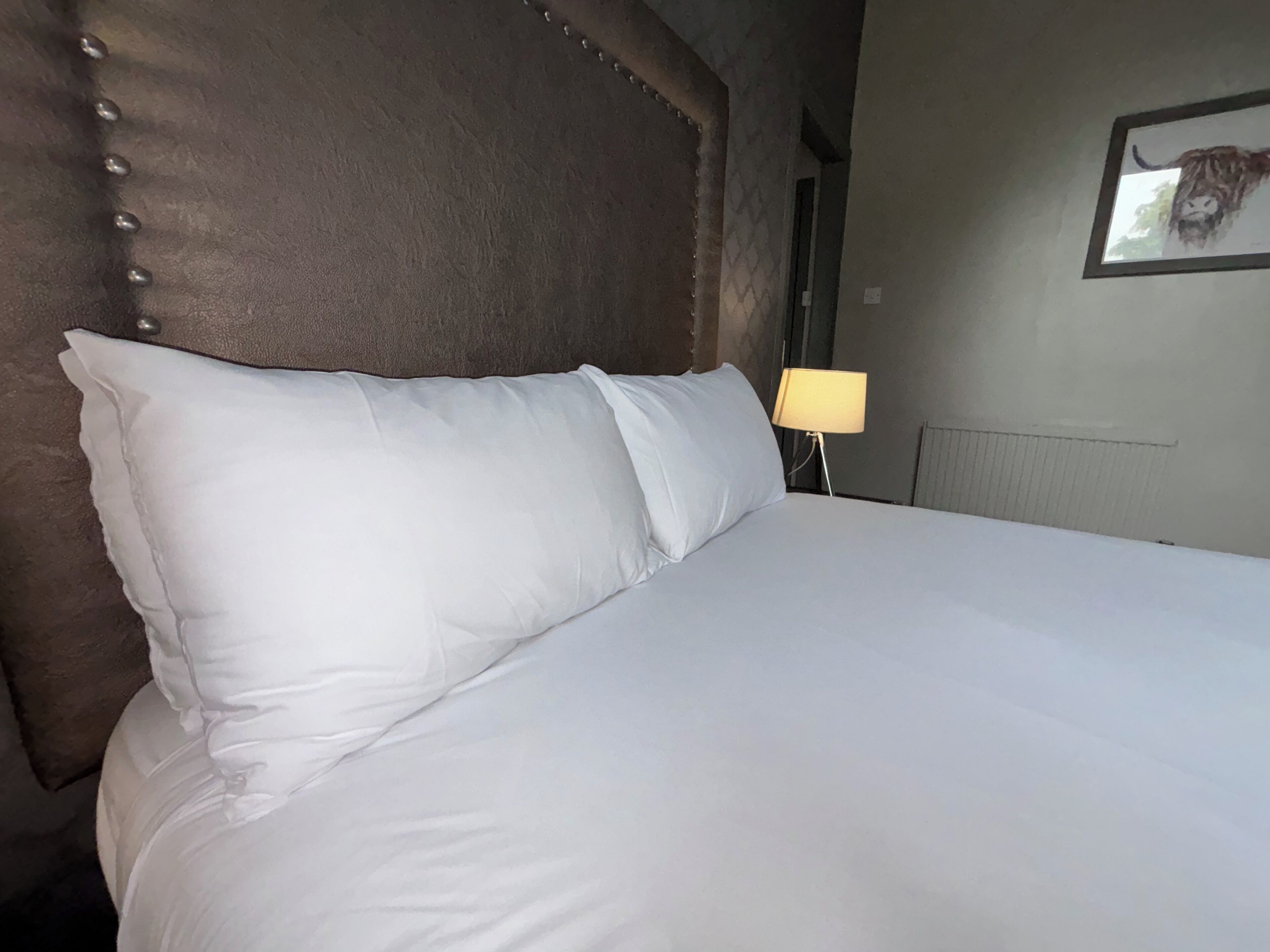 Una cama bien hecha con sábanas blancas y un cabecero con diseño capitonado.