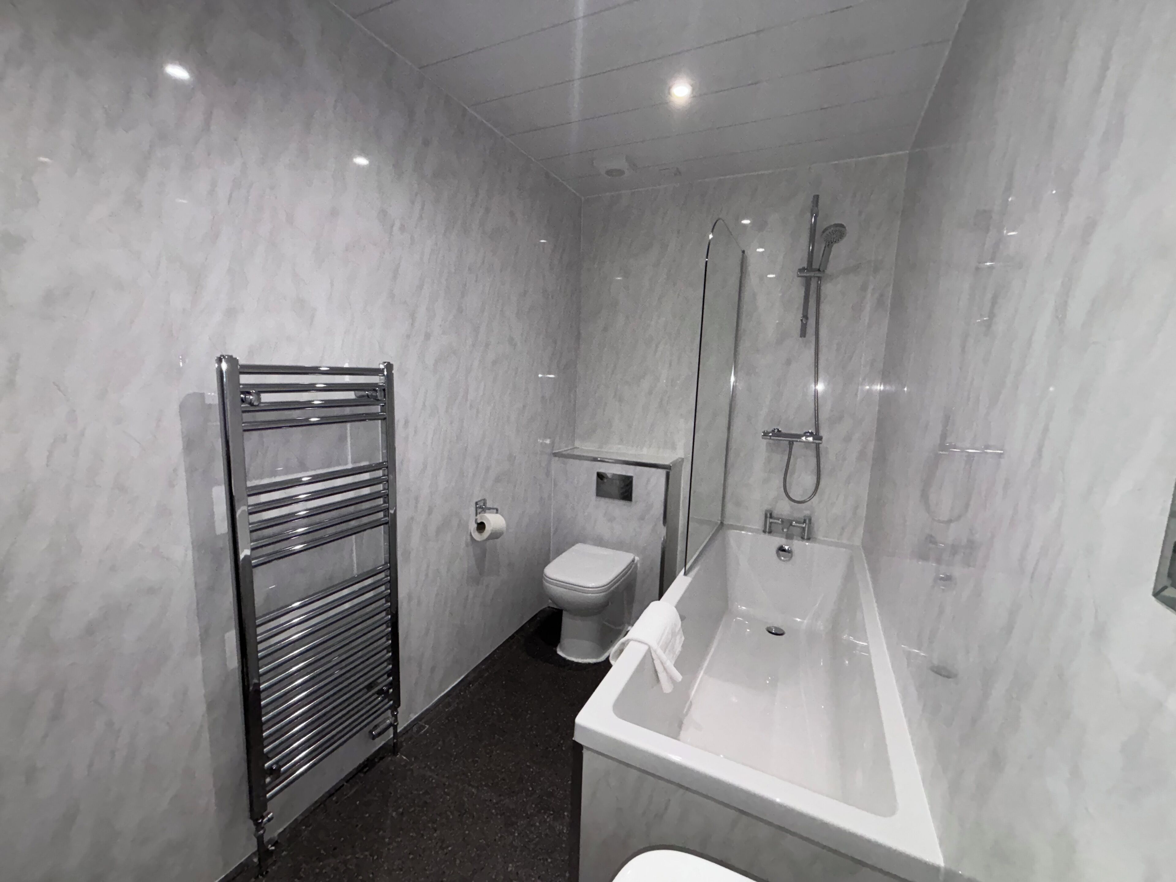 Un baño moderno con ducha de vidrio, una bañera blanca, un inodoro y un perchero para toallas.