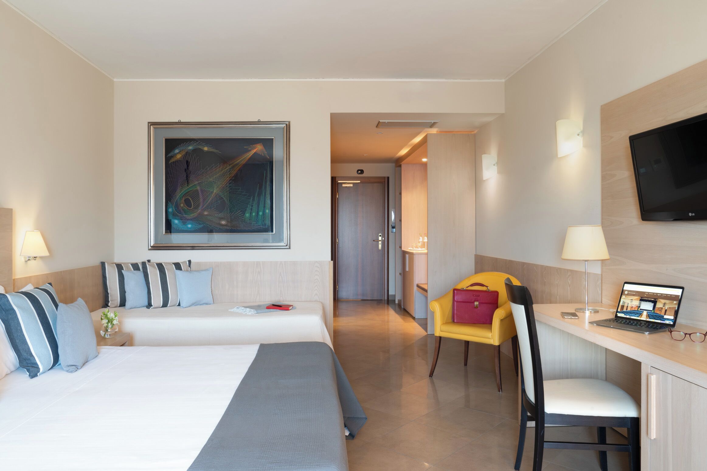 Una camera d'albergo con un letto, una scrivania con un portatile, una televisione e un quadro appeso al muro.