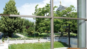 A dining area with wicker chairs and white tables, large windows offering a view of a park and a building with a dome. - Domus Pacis Assisi (Assisi)