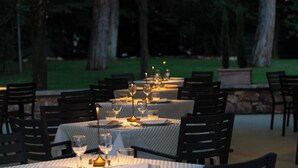 An outdoor dining area with tables set for two, each with a candle centerpiece, surrounded by chairs. - Domus Pacis Assisi (Assisi)