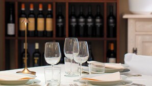 A dining table set with plates, glasses, and cutlery, with a wine rack in the background. - Domus Pacis Assisi (Assisi)