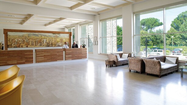A spacious lobby with a reception desk, seating area, and large windows offering a view of the outdoors. - Domus Pacis Assisi (Assisi)
