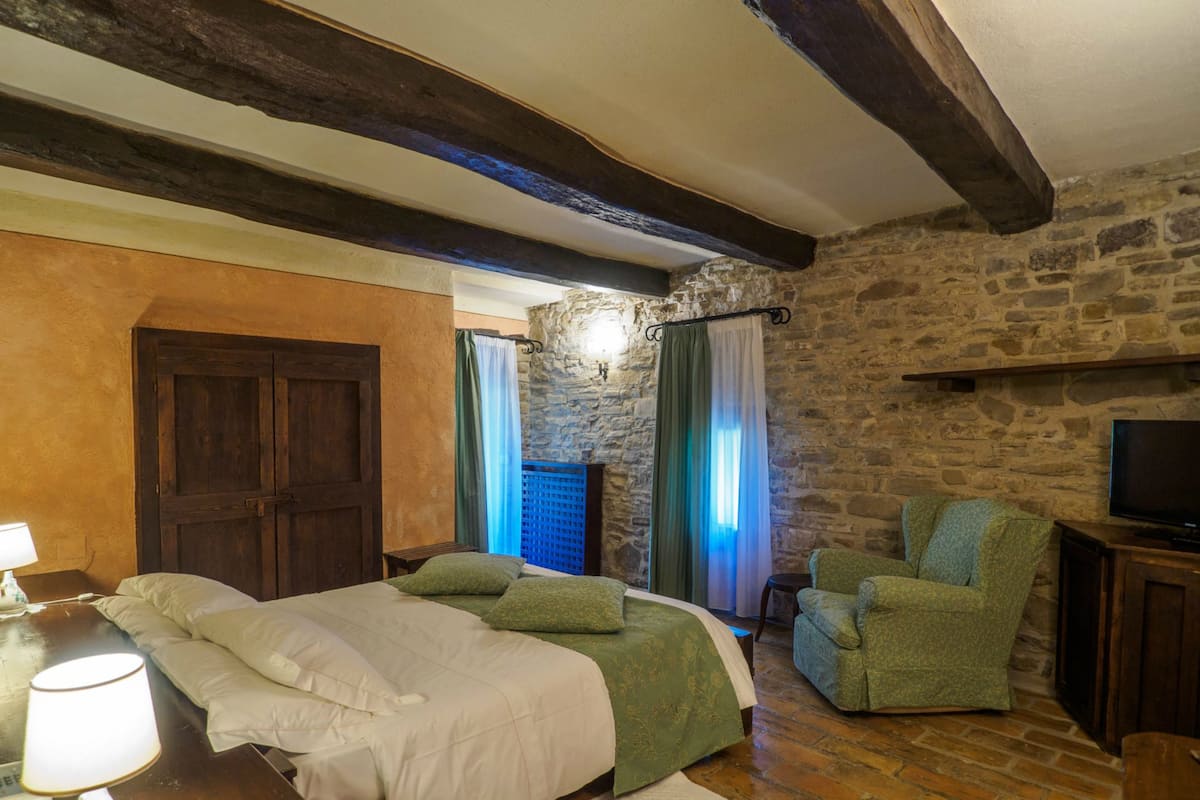 Ein Schlafzimmer mit einem großen Bett, einem Sessel, einem Fernseher und Steinwänden.