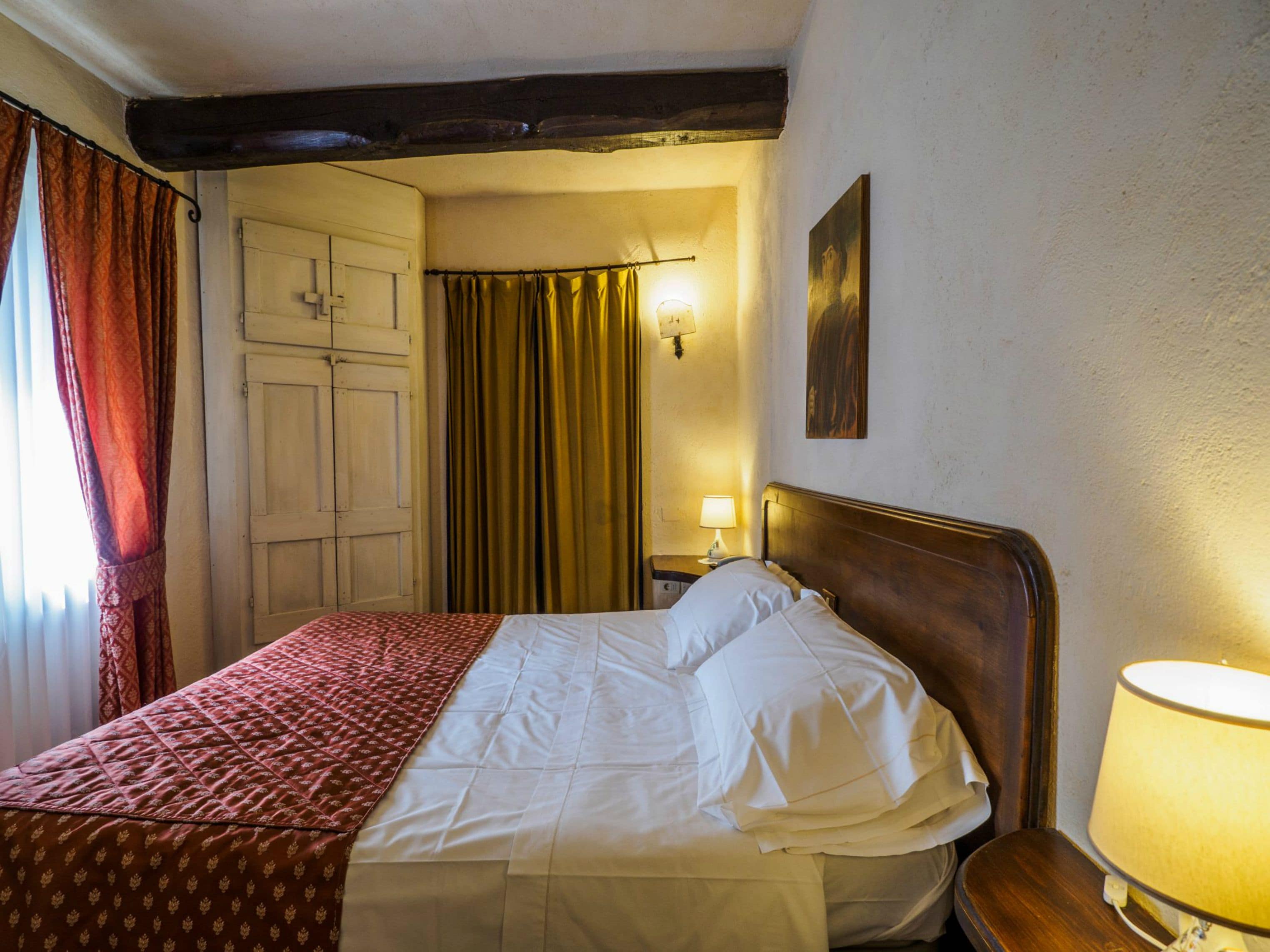 Een hotelkamer met een bed, een nachtkastje met een lamp, een kledingkast en een gordijn.