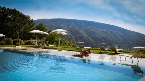Un área de piscina con sillas de descanso y sombrillas, rodeada de exuberante vegetación y un paisaje de montañas.