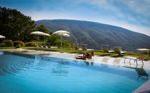 Un espace piscine agrémenté de chaises longues et de parasols, entouré d’une végétation luxuriante et avec une chaîne de montagnes en toile de fond.