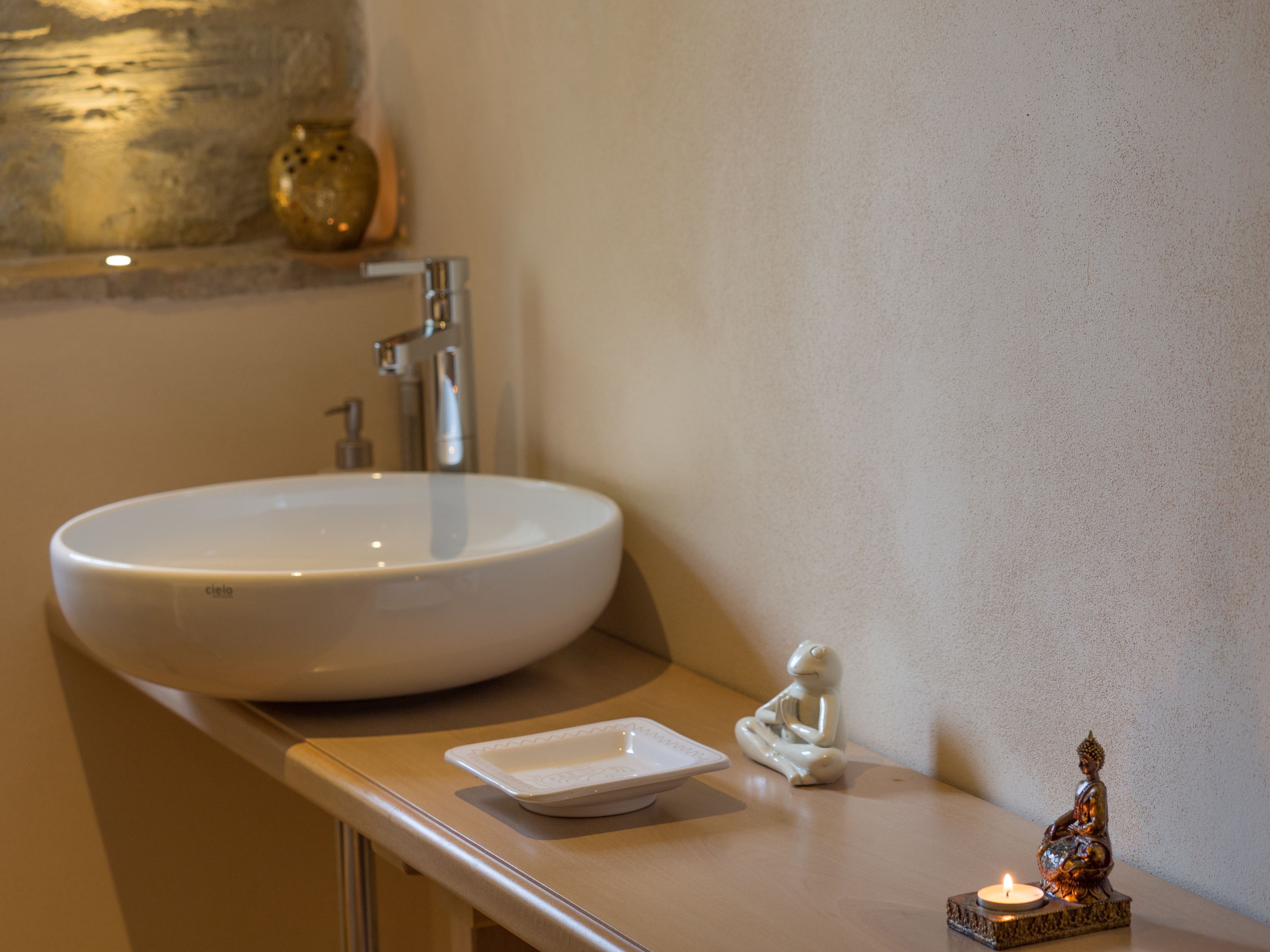 A bathroom with a white sink, a small white tray, and a Buddha statue.