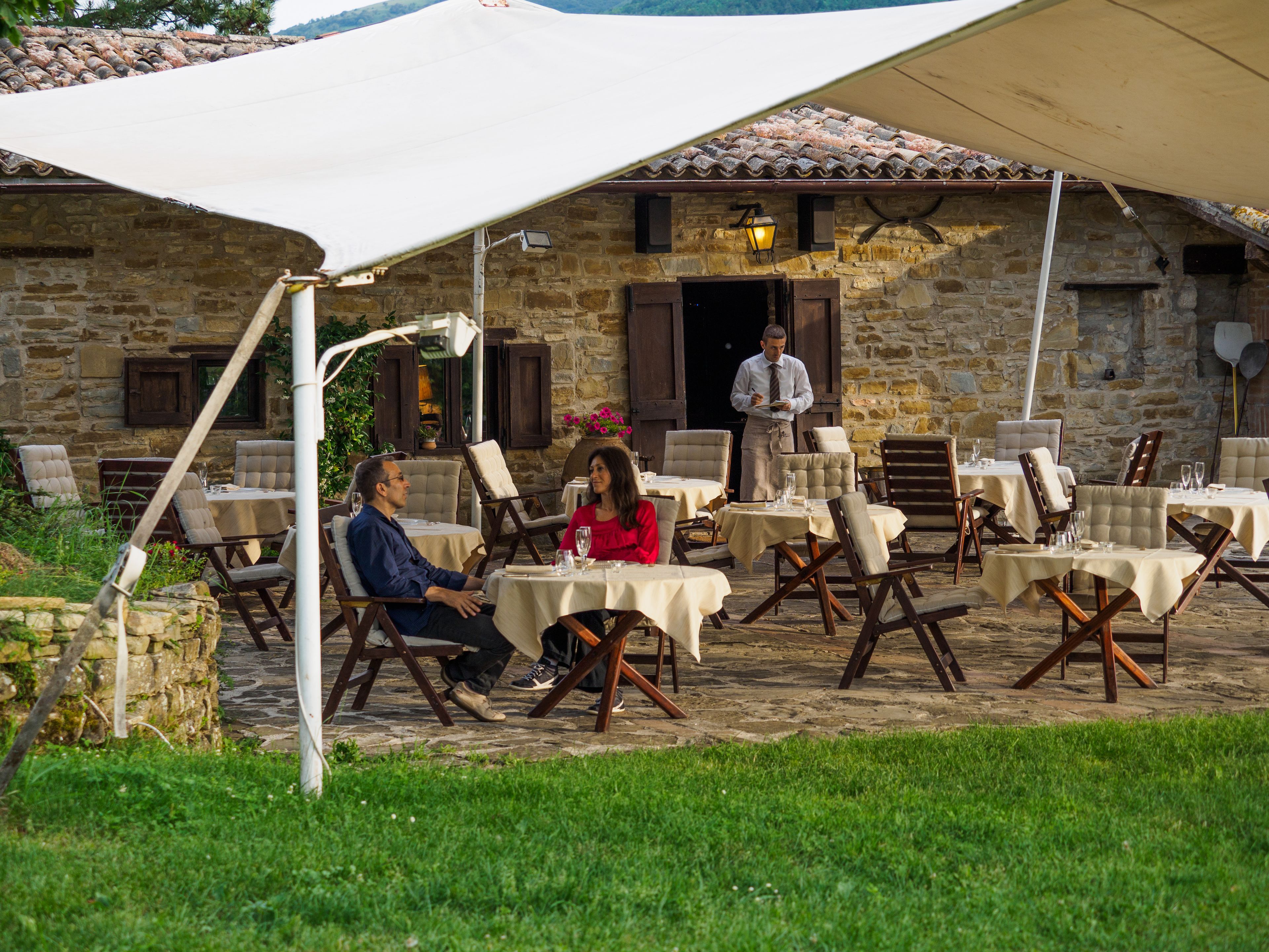 An outdoor seating area with stone walls and tables, chairs, and a person standing in the background.