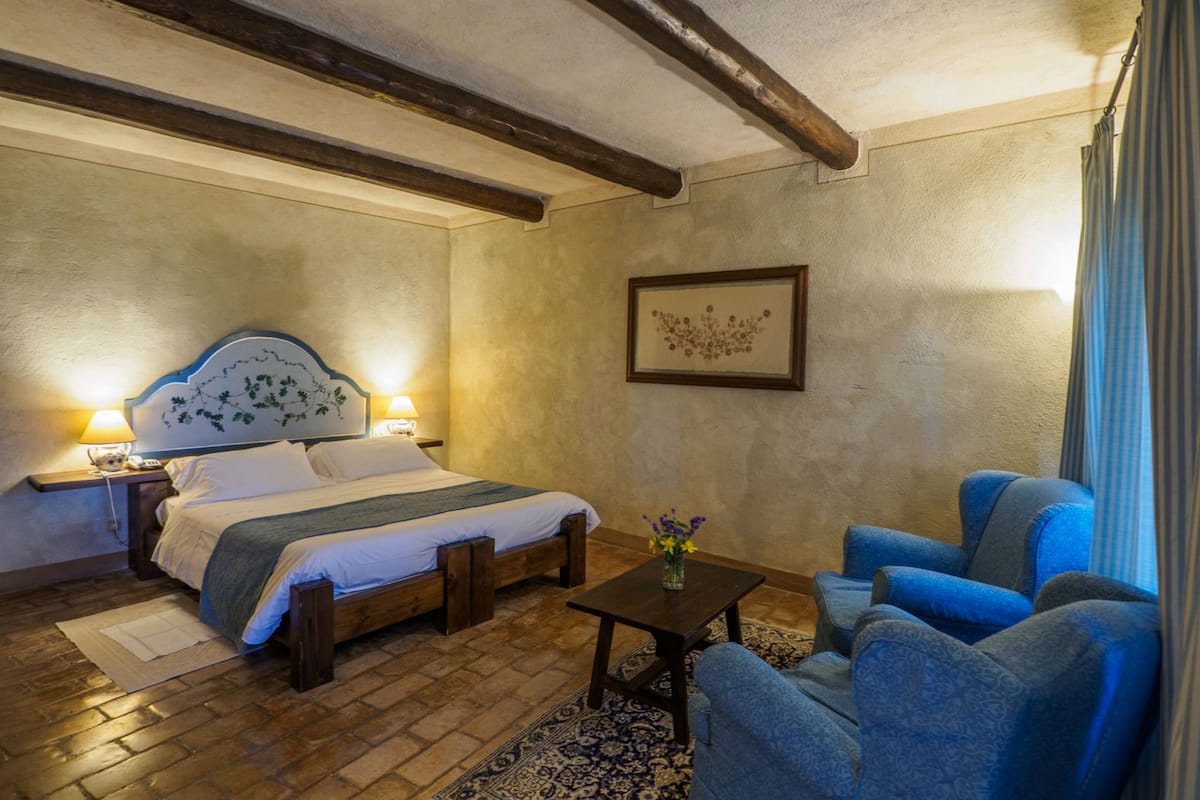 Ein Schlafzimmer mit einem Holzbett, zwei Nachttischlampen, einem kleinen Tisch mit einer Vase und einem blauen Sessel.