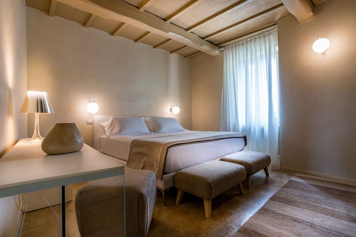 Ein modernes Schlafzimmer mit Bett, Nachttischlampen, Schreibtisch und einem Fenster mit Vorhängen.