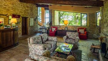 A rustic interior with stone walls, wooden beams, and floral upholstered furniture.