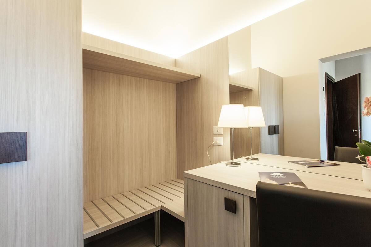Una habitación de hotel moderna con un banco de madera, un escritorio con lámpara y un espejo.
