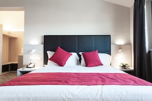 A modern hotel room with a large bed, two red pillows, a white comforter, and a dark headboard. There are bedside tables with lamps and a phone. - Hotel Los Angeles (Assisi)