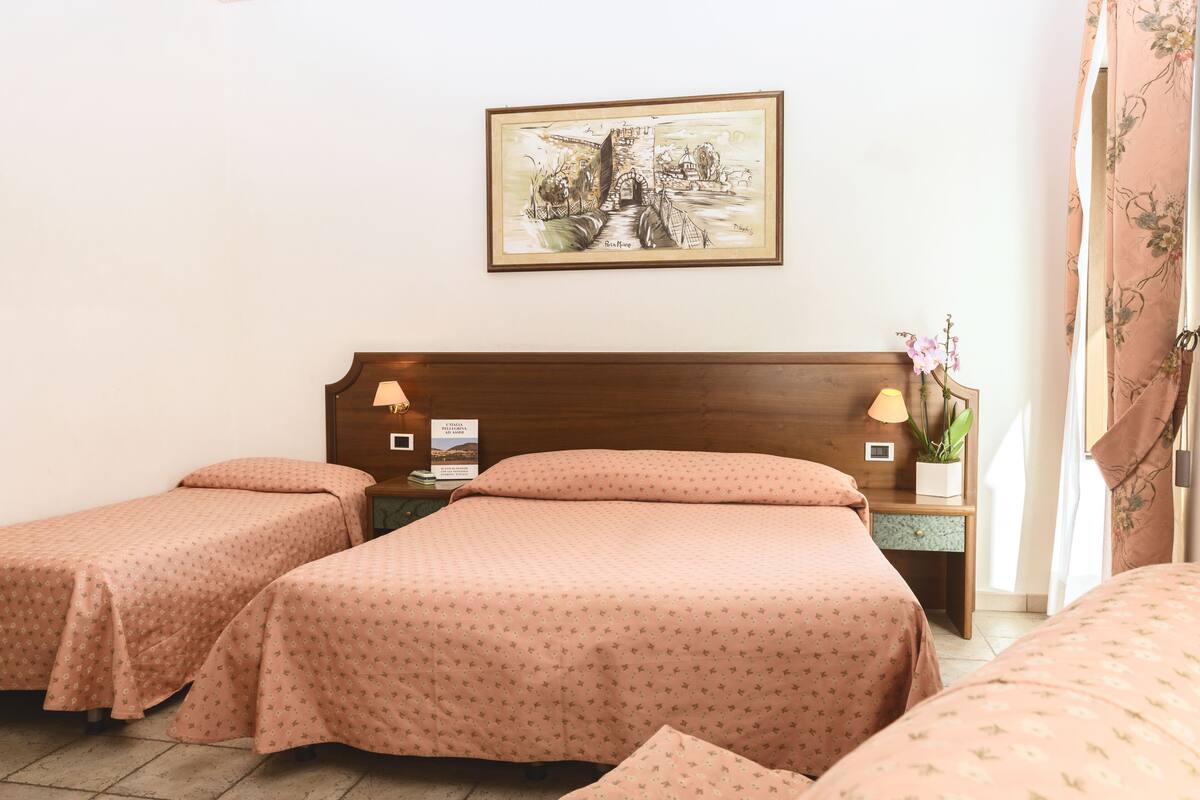 A hotel room with two single beds, a wooden headboard, a nightstand with a lamp, a framed picture on the wall, and a window with curtains.
