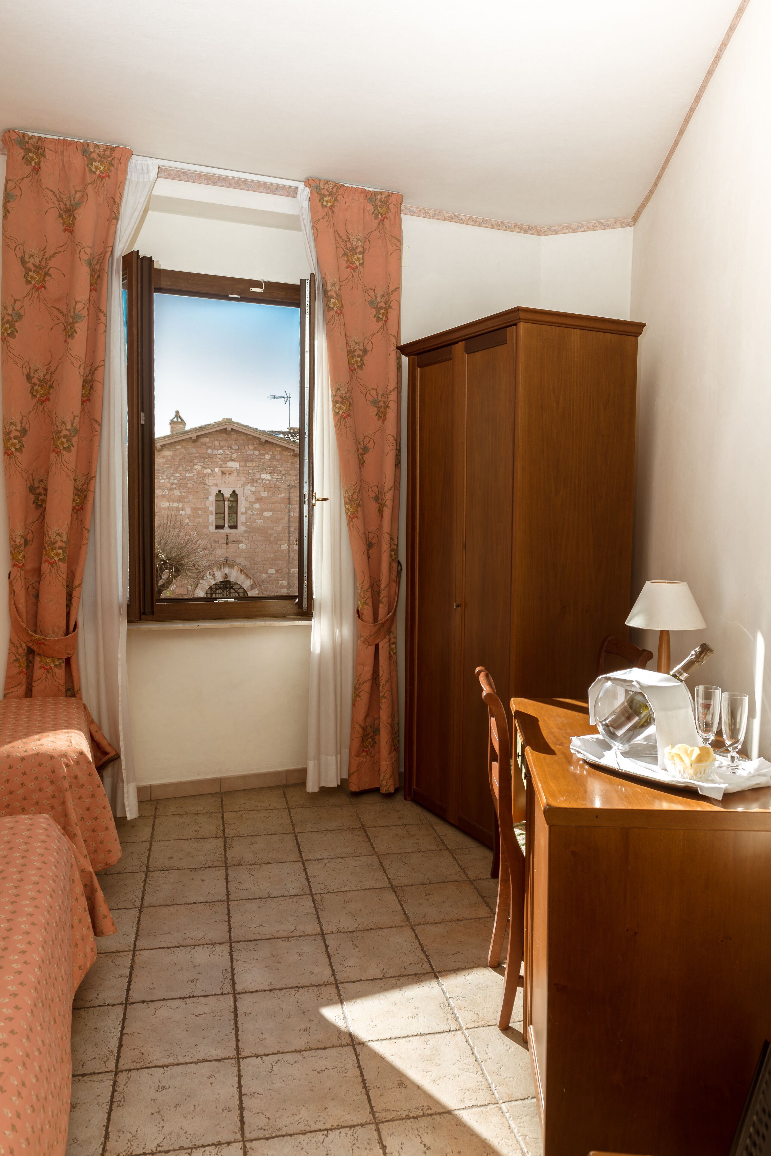 A room with a window, a wooden cabinet, a table with a lamp, and a bed.