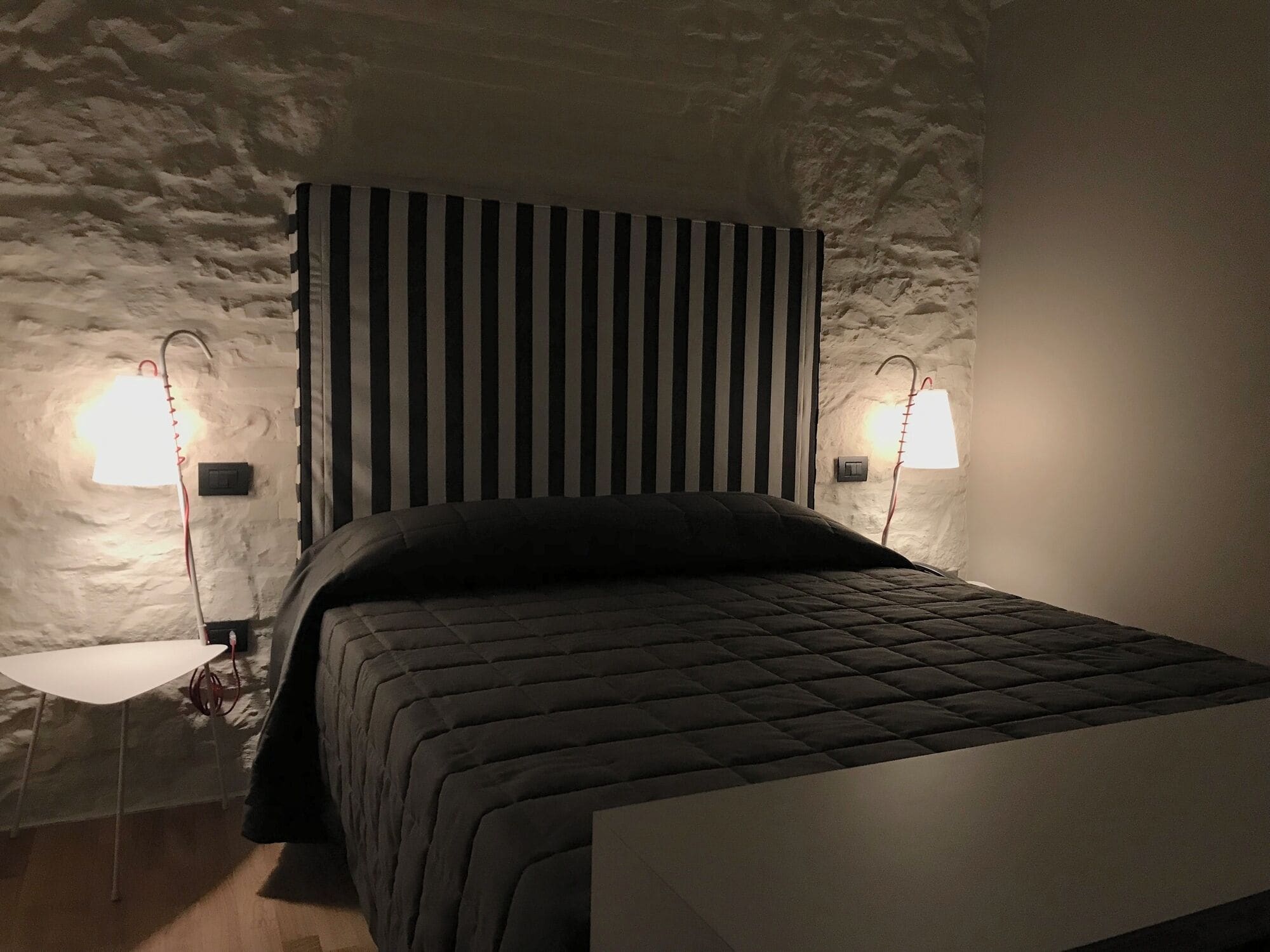 A bedroom with a bed, a bedside table, a lamp, and a wall with a textured pattern.