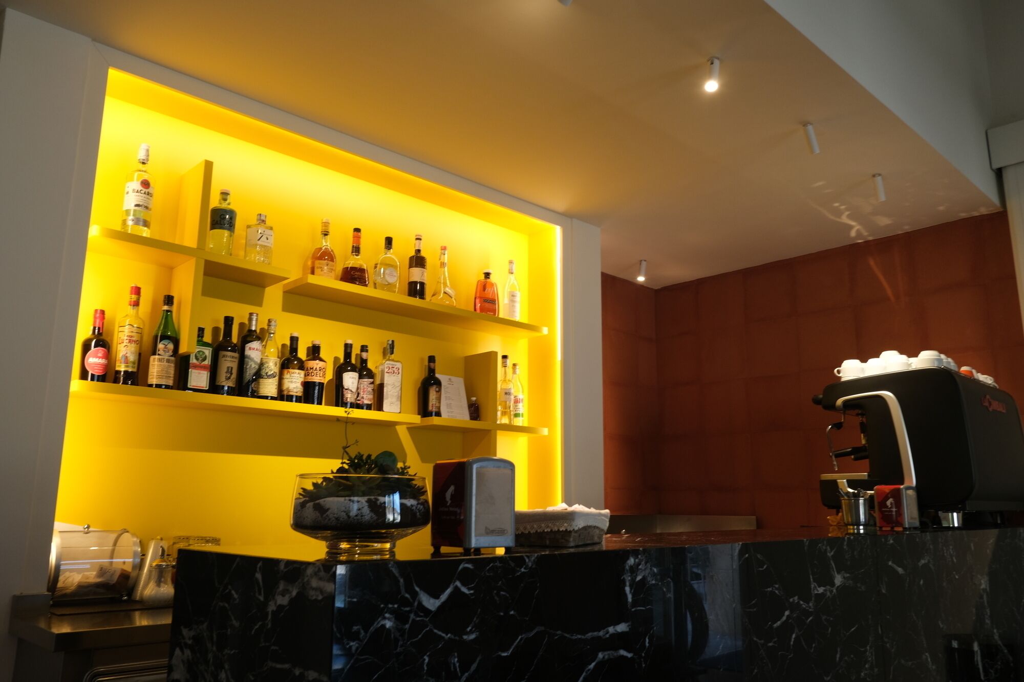 A bar area with shelves of liquor bottles, a coffee machine, and a marble countertop.