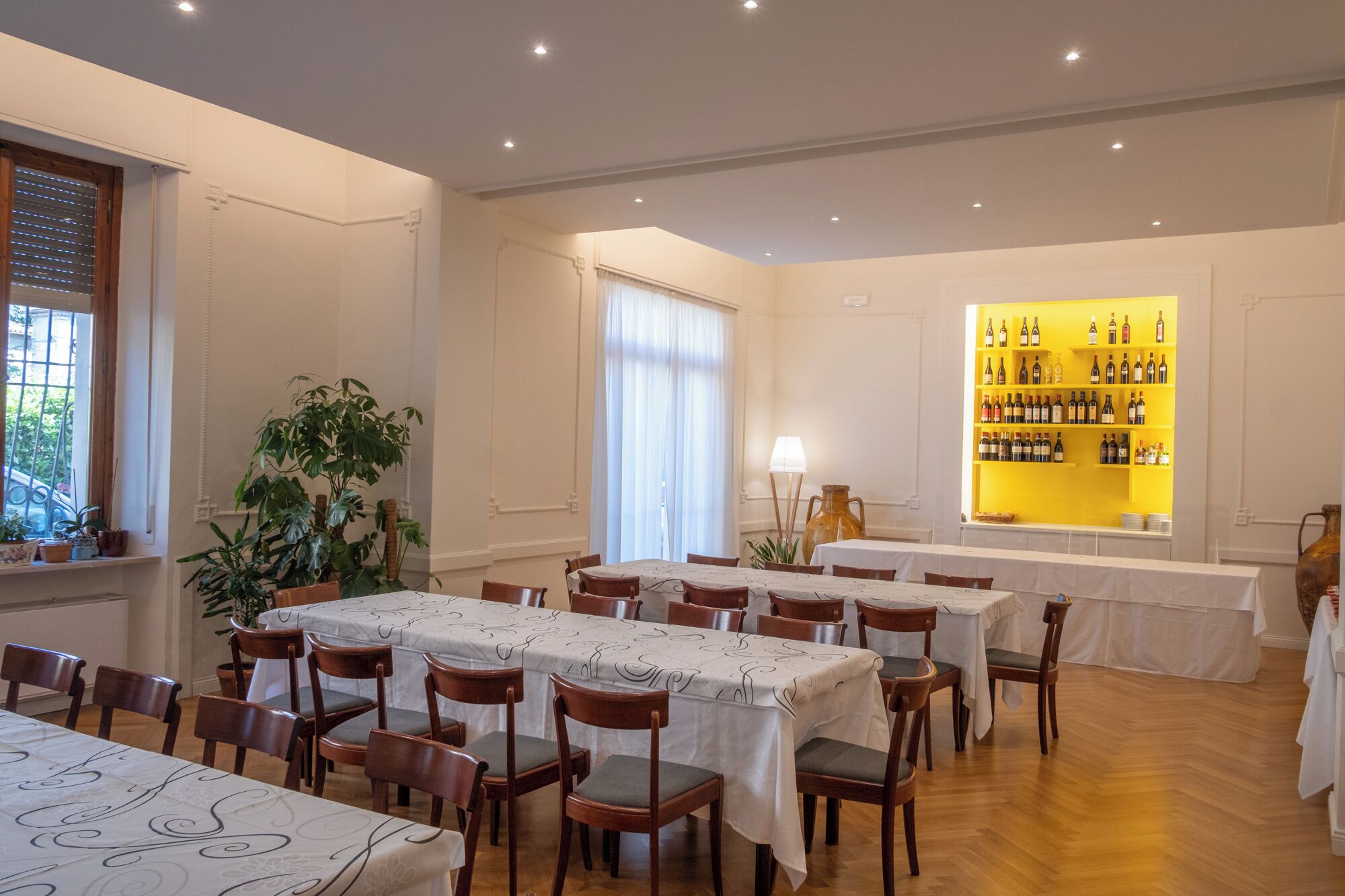Un restaurant doté de nombreuses tables et chaises, d’un présentoir à vin et de plantes en pot.