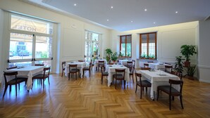 A spacious dining area with multiple tables and chairs, large windows, and potted plants. - Hotel Moderno (Assisi)