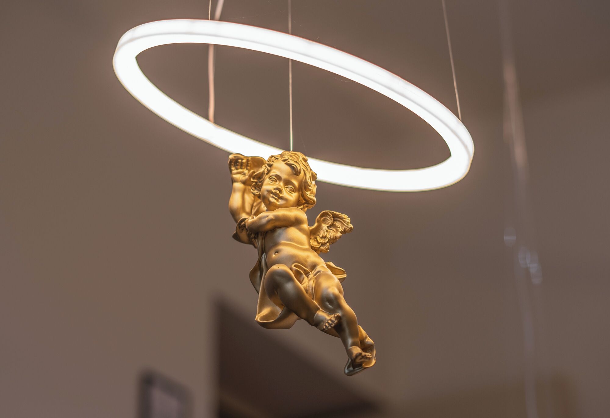 A golden angel sculpture suspended by a white circular light fixture.