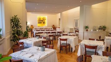 Un restaurante con varias mesas y sillas, una exhibición de vinos y plantas en macetas.