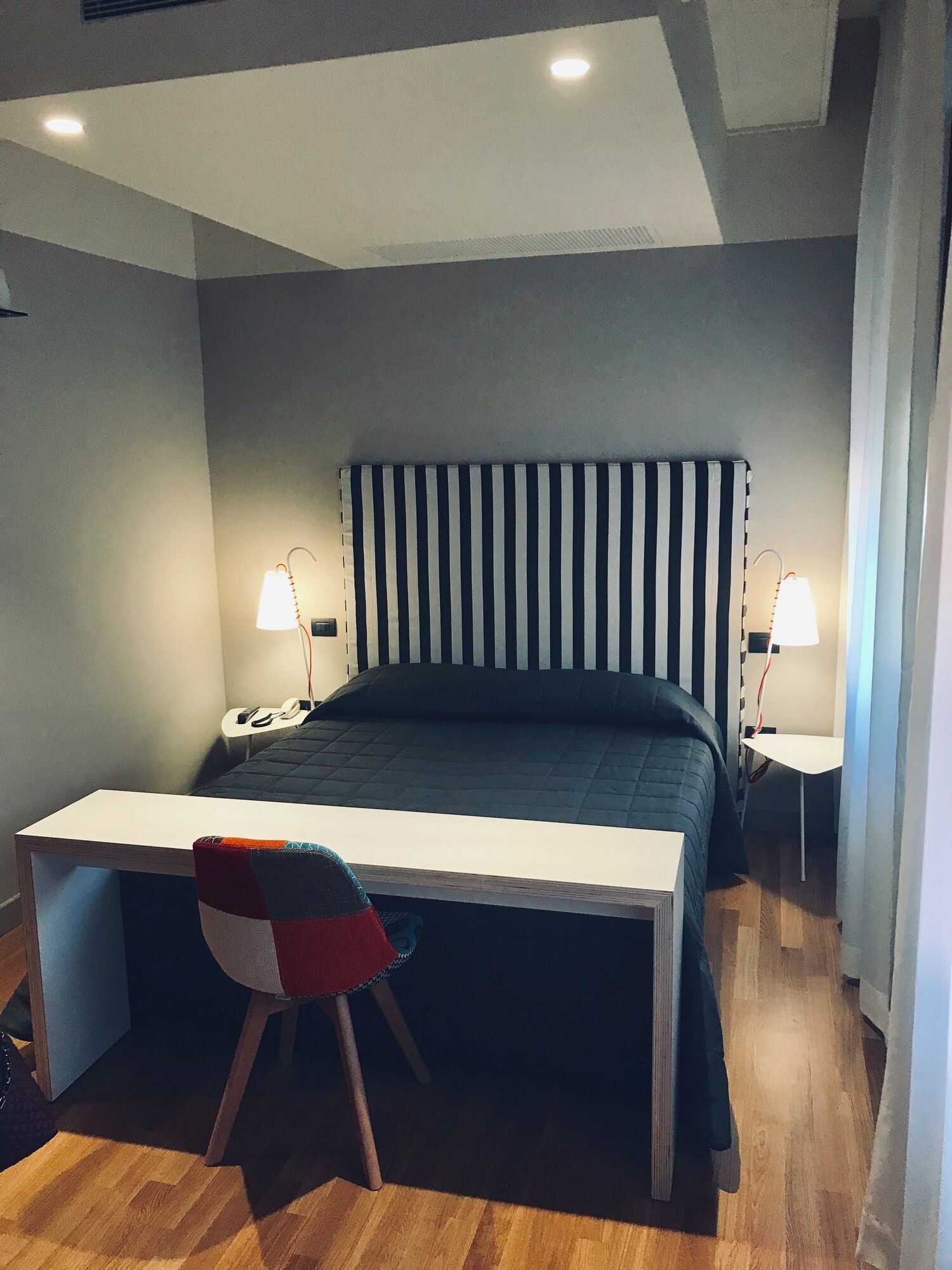 A bedroom with a bed, a desk, and two bedside lamps.