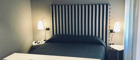 A bedroom with a bed, a desk, and two bedside lamps.