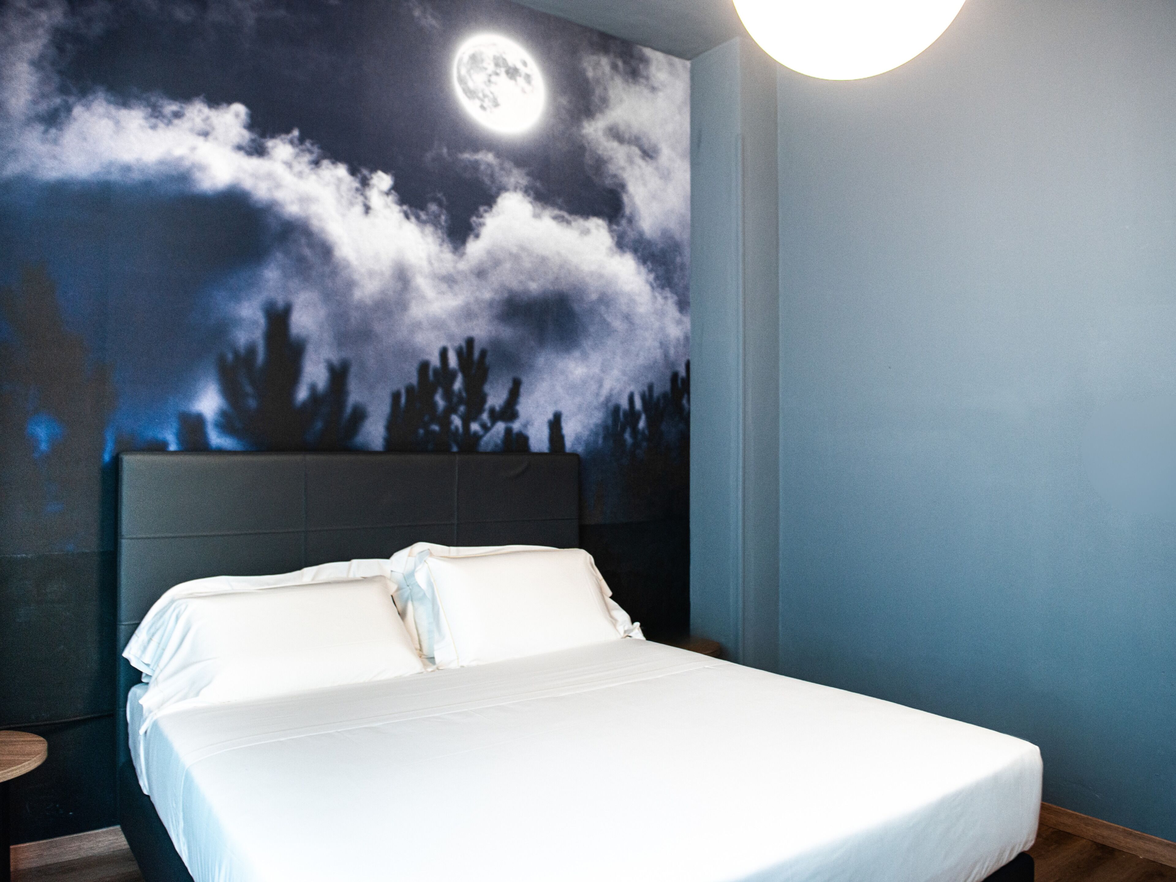 Un dormitorio con cama, un mural del cielo nocturno en la pared y una lámpara redonda.
