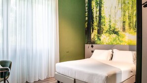 A bedroom with a bed, a chair, a painting of a forest, and a green wall.
