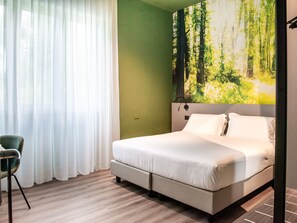 A bedroom with a bed, a chair, a painting of a forest, and a green wall.