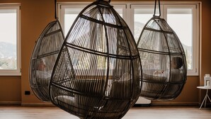 A room with three hanging wicker chairs, a small white table, and a view of mountains through large windows. - Hotel Del Lago 1934 & SPA (Terni)