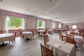 A spacious dining area with multiple tables and chairs, large windows with curtains, and a clean, light-colored floor. - Hotel Del Lago 1934 & SPA (Terni)