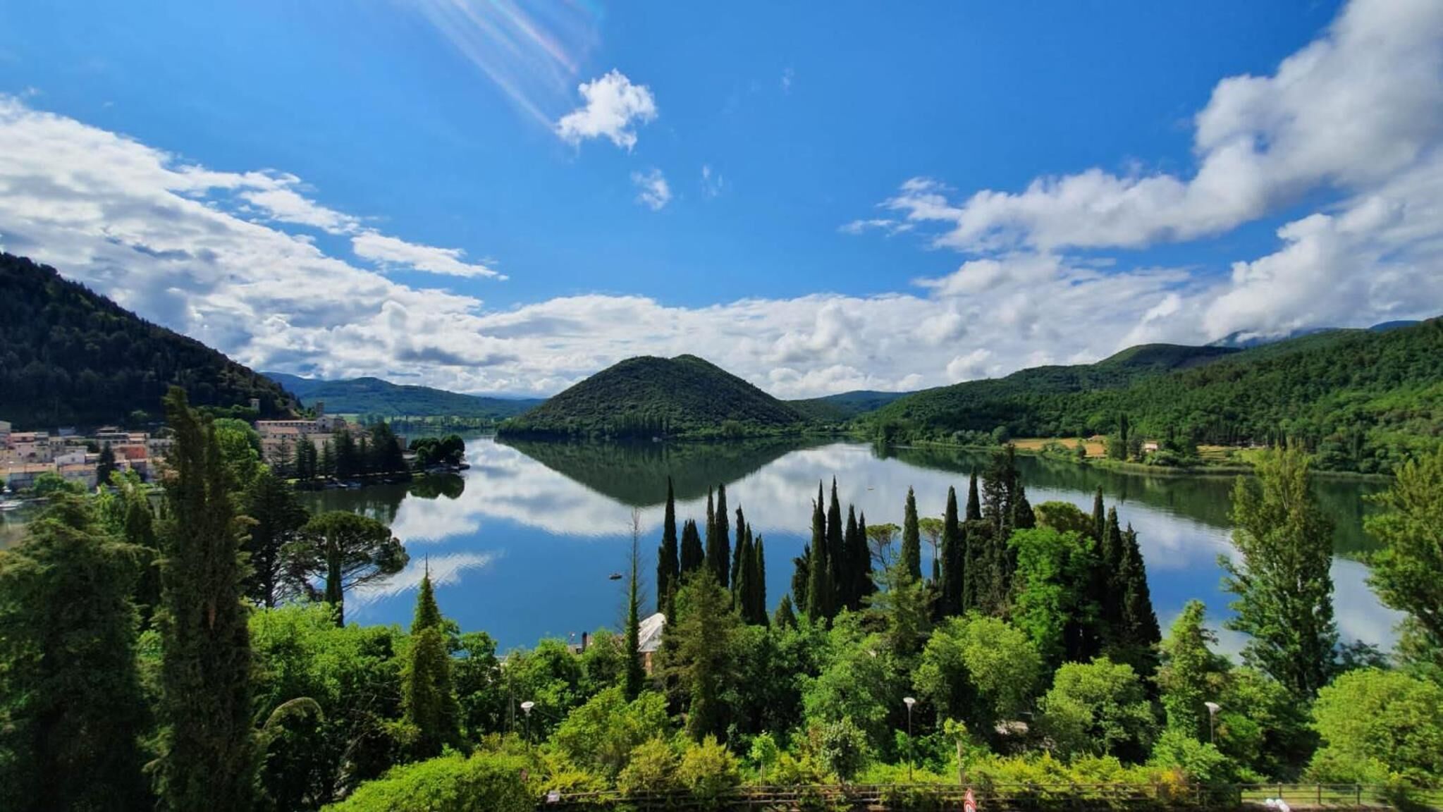 A lake surrounded by hills, with a town in the foreground and a mountain in the background.