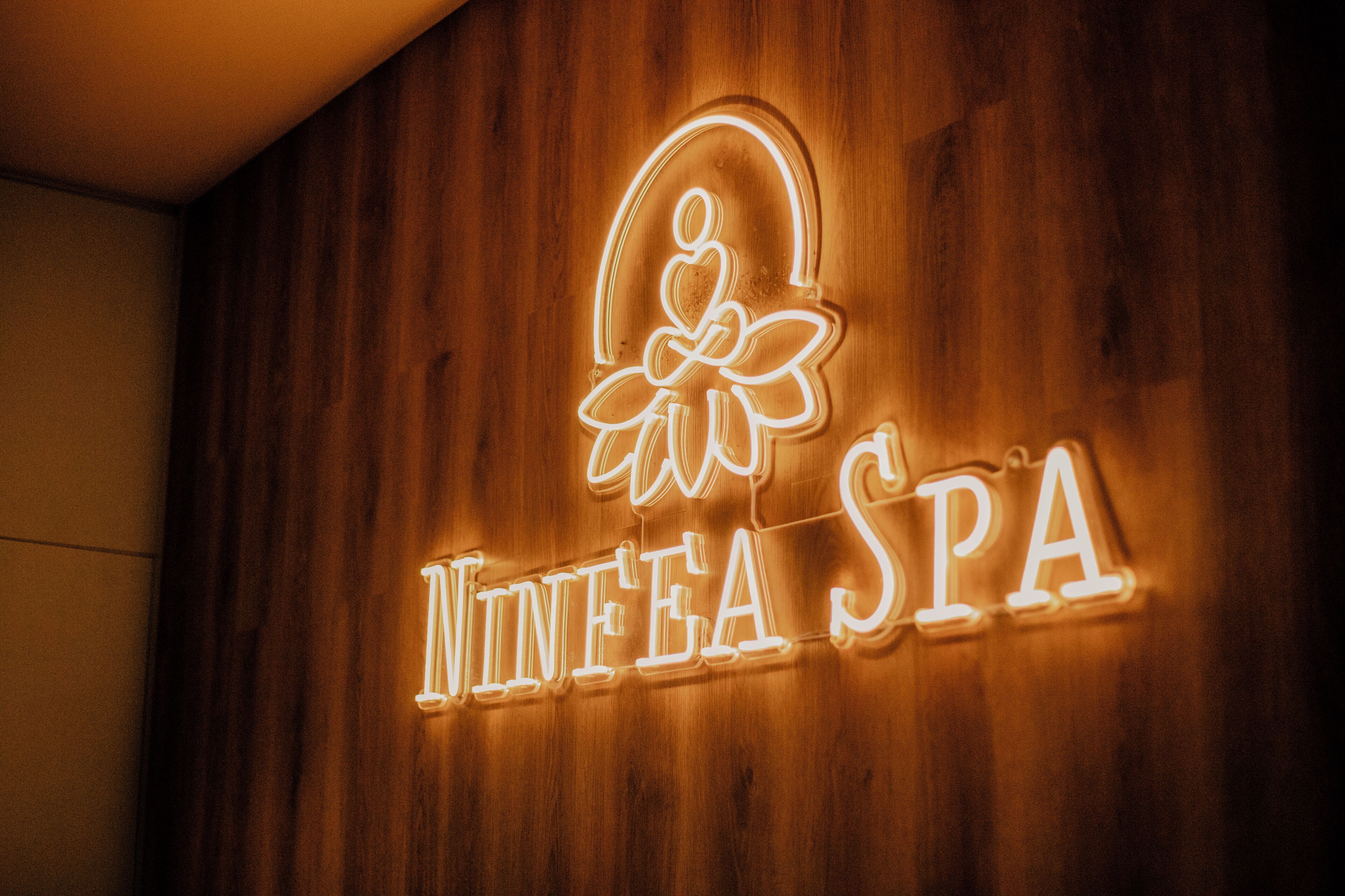 A neon sign with the text "Ninetea Spa" on a wooden wall.
