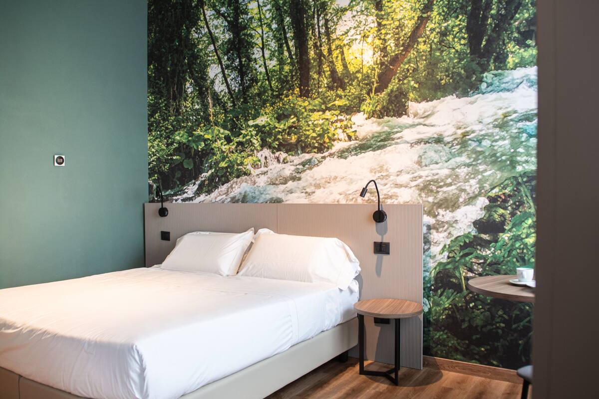 Ein Schlafzimmer mit einem Bett, einem kleinen Tisch und einer Wandmalerei mit Waldbild.