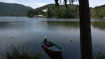 A calm lake with a small boat tied to a tree, surrounded by lush greenery and hills in the background.