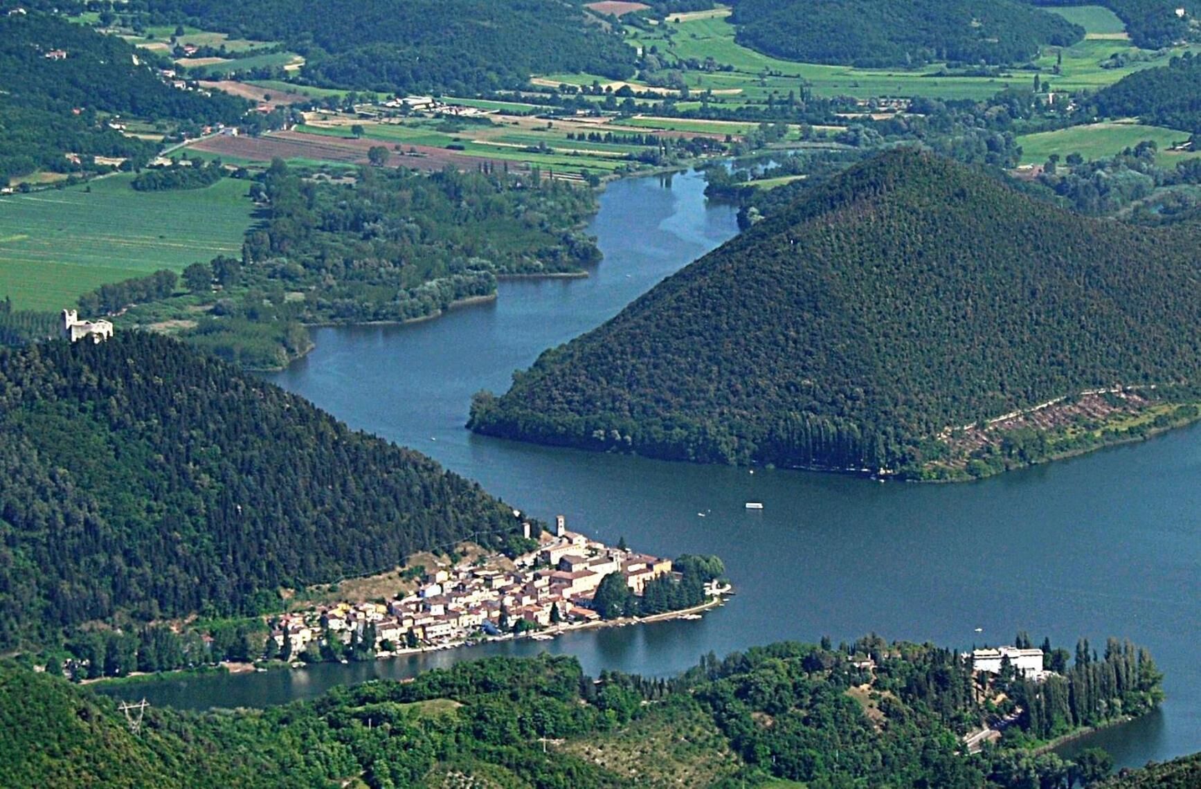 A lakeside town with a central cluster of buildings, surrounded by forested hills and a river.