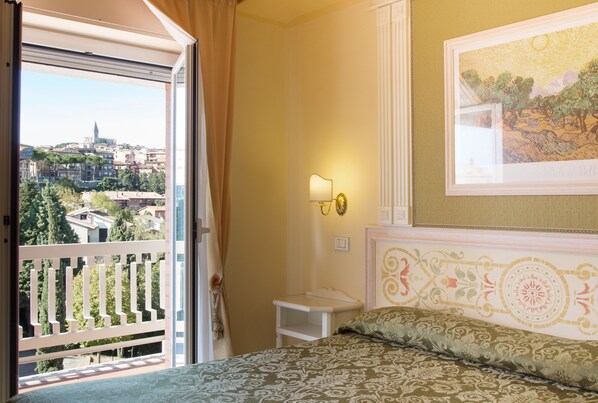 A hotel room with a balcony, a bed with patterned bedding, a nightstand, a wall-mounted lamp, and a framed artwork.