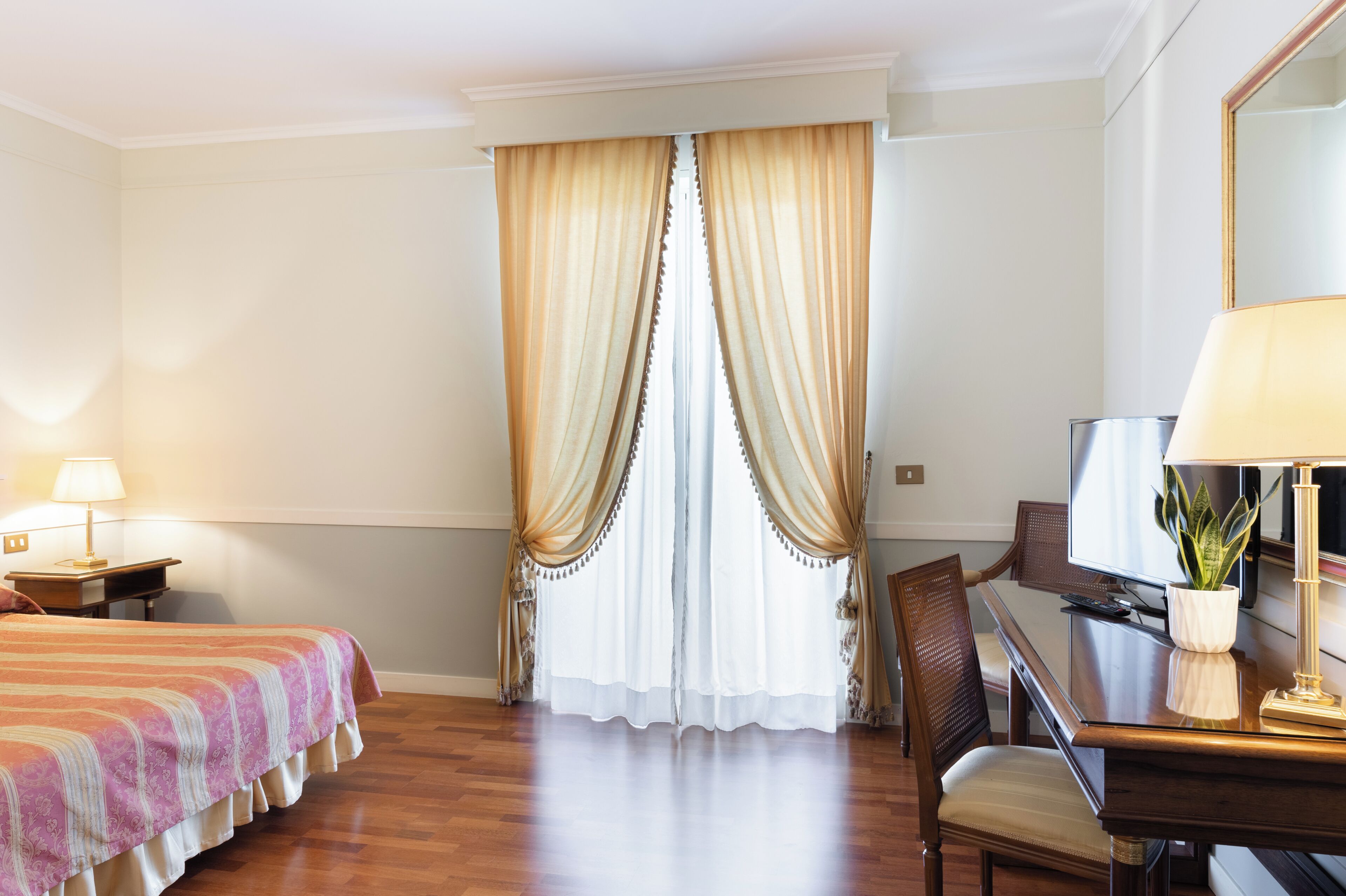 A hotel room with a bed, a desk, a chair, a television, and a window with curtains.