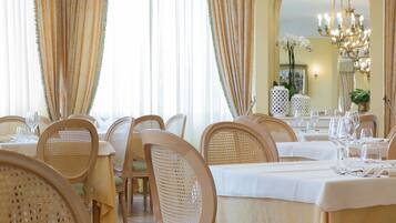 A dining area with tables set for service, wicker chairs, and a chandelier.