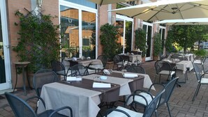 An outdoor patio area with tables and chairs, some covered by umbrellas, and potted plants. - Tuder (Todi)