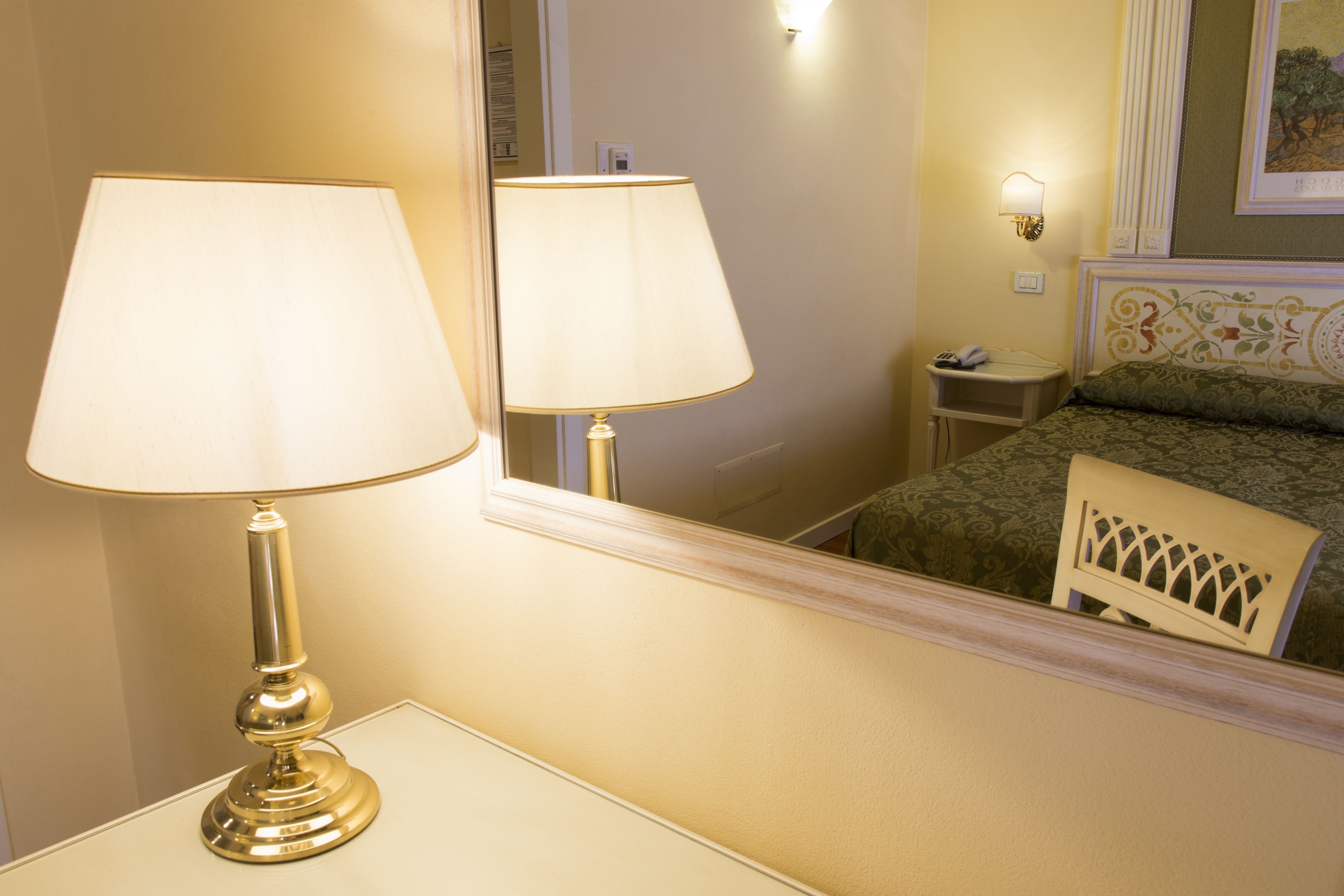 Un dormitorio con mesita de noche, lámpara, una silla y cama con colcha estampada.
