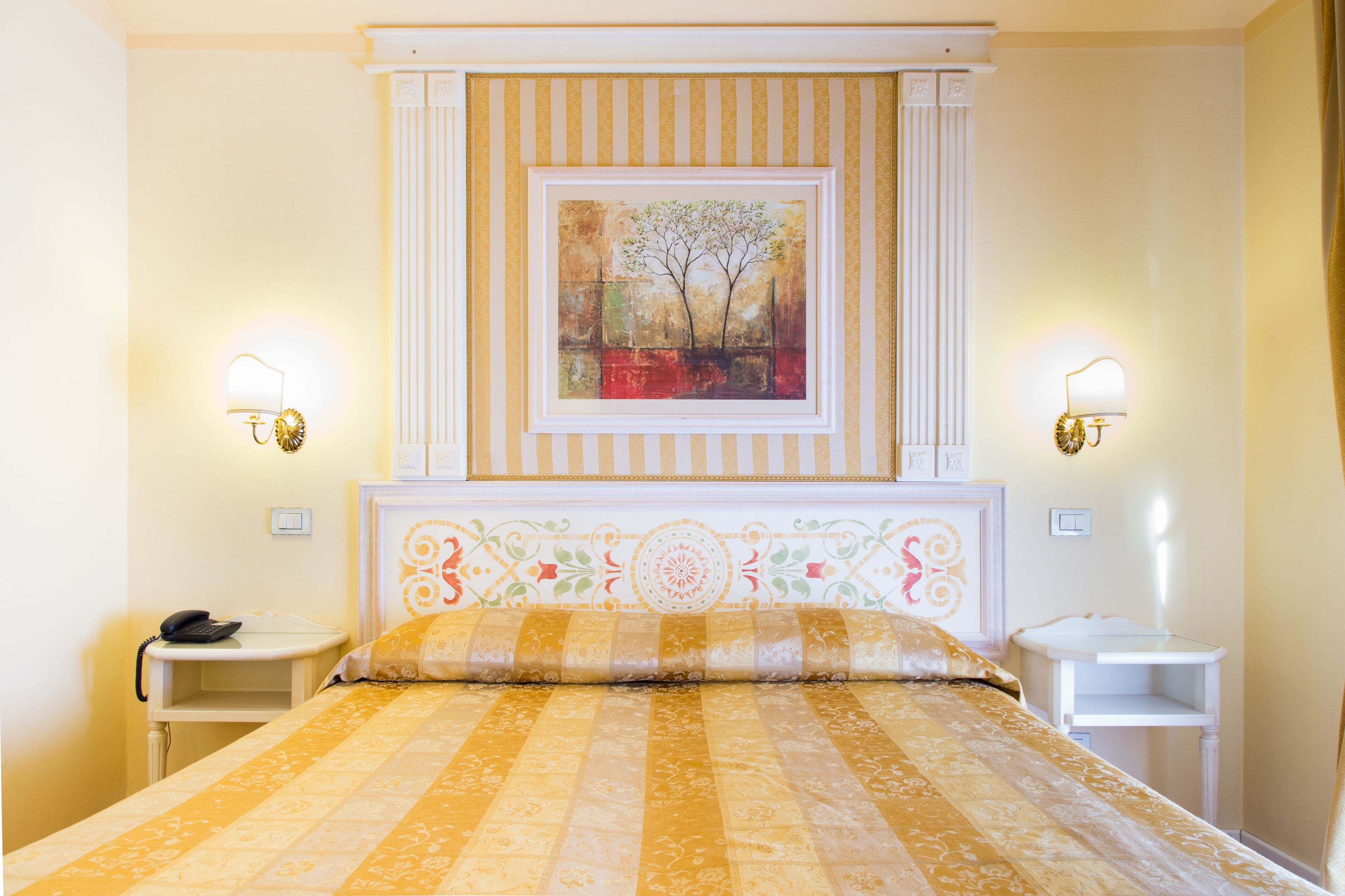 Habitación de hotel con cama, dos mesitas de noche, teléfono y un cuadro sobre la cama.