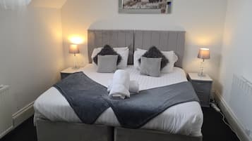 Una cama bien hecha con cabecera gris, dos lámparas de noche y un cuadro en la pared.